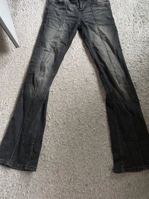 Grå slitna bootcut jeans - Säljer ett par grå/ svarta  bootcut jeans med slitningar och ljusare partier längs benen. Jeansen har klassisk femficksmodell och dragkedja fram. Perfekta för en avslappnad och trendig look.