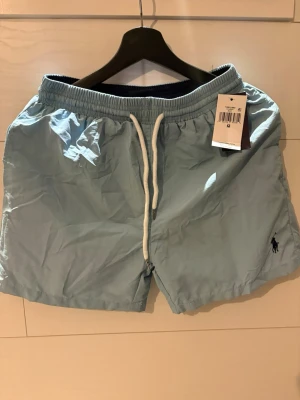 Ralph lauren badbyxor M - Snygga ljusblå badbyxor med vit dragsko och resår i midjan. Klassisk modell med diskret logga broderad på ena benet. Perfekta för stranden eller poolen, tillverkade i snabbtorkande material.