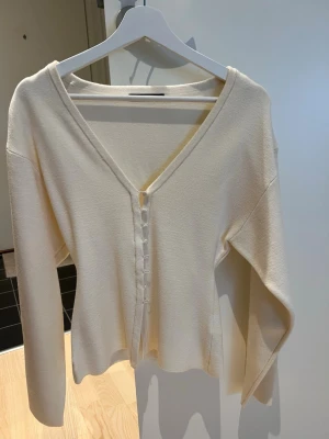 Vit kofta från Gina Tricot - Stilren vit kofta från Gina Tricot med v-ringning och knappar framtill. Koftan har långa ärmar och är tillverkad i ett mjukt lite tjockare material.