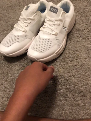 On cloud skor  - Snygga vita sneakers från On med ventilerande meshpaneler och klassisk snörning. Skorna har en chunky sula och diskret logga på sidan. Insidan är ljusblå för extra stilpoäng. Perfekta för dig som gillar sportig och clean look.