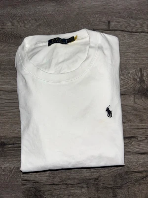 Vit t-shirt från Polo Ralph Lauren - Klassisk vit t-shirt från Polo Ralph Lauren med rund hals och den ikoniska broderade loggan i svart på bröstet. Tillverkad i mjuk bomull för en skön känsla och enkel stil som funkar till allt.  Den är helt ny och oanvänd , men jag råkade ta bort tagen !