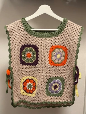 Handmade Crochet Granny Square Vest - Handmade Crochet Granny Square Vest  60's vintage-style crochet vest featuring four colorful granny squares on a neutral beige base. Made with soft yarn in earthy tones of green, orange, purple, and yellow. Ties on the sides for an adjustable fit. Perfect layered over a t-shirt or dress for that cozy, boho look. Size: One size (fits S-M best) Condition: New/unused