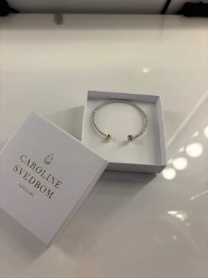 Caroline Svedbom armband - Helt oanvänt silvrigt Caroline Svedbom armband med gulskimrande stenar i nyskick. Nypris är 595kr