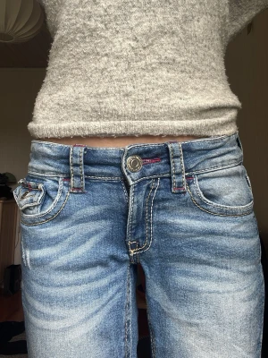 Blå bootcut jeans med hål i knäna och röda detaljer - Blåa bootcut jeans från Gina tricot med hål vid knäna, knappar på fickorna och röda detaljer.