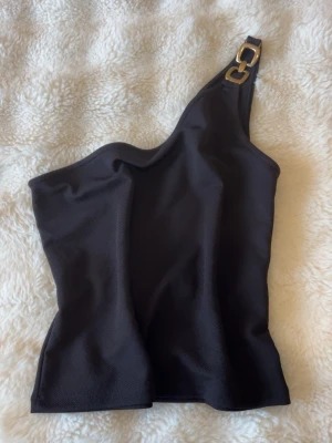 oneshoulder topp - gulddetalj - Använd 1 gång, Snygg svart oneshoulder topp med guldfärgad metallring på axelbandet. Toppen har en tight passform och ärmlös design.
