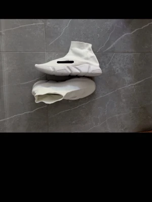 Vita Balenciga skor  - Säljer ett par helvita Balencgia sneakers med stickad ovandel i strumpmodell och chunky sula. Skorna har en modern, minimalistisk look och är tillverkade i textil med en grov, mönstrad yttersula i gummi. Perfekta för dig som gillar streetwear och vill ha något unikt.