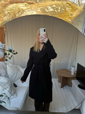 Svart lång kappa - Stilren svart kappa i lång modell med knytskärp i midjan. Perfekt nu till våren!