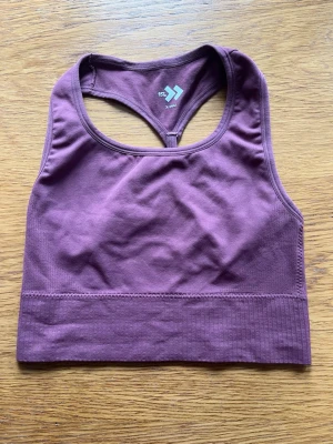 Lila tränings topp från Lager 157 strl XS - Säljer en lila tränings topp från Lager 157 i stretchigt material med brottarrygg och bred resår under bysten. Toppen har en enkel, sömlös design och är perfekt för träning eller chill. Material 92% nylon, 8% elastan. Storlek XS.