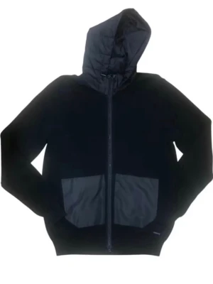 Svart cardigan med dragkedja och fickor - Säljer en svart Cardigan med dragkedja och två stora fickor framtill. Huvan är fodrad och materialet ser ut att vara en mix av bomull och syntet. Ribbstickade muddar vid ärmar och nederkant. Perfekt för en chill och stilren look. OBS den är använd endast 4 ggr.