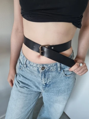 Svart skärp i skinn med metallspänne handgjord  - Snyggt svart skärp i skinn med ett robust metallspänne. Bältet har en klassisk design och flera hål för justerbar passform. Perfekt att styla till jeans eller kjol för en cool och enkel look. Handgjord