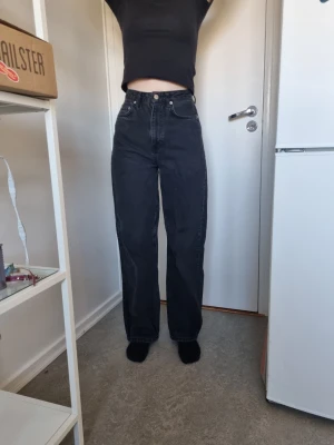 Svarta raka jeans med hög midja - Säljer ett par svarta jeans med rak passform och hög midja. Jeansen har klassiska fem fickor och stängs med knapp och dragkedja. Materialet är kraftig denim som ger en snygg vintagekänsla. Perfekta till en enkel topp eller hoodie.