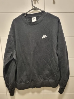 Svart Nike sweatshirt med RUN-tryck - Svart sweatshirt från Nike med klassisk vit logga på bröstet och stort rött RUN-tryck på ryggen. Tröjan har rund hals, ribbade muddar och är tillverkad i mjukt bomullsmaterial. Perfekt för dig som gillar sportig streetstyle.