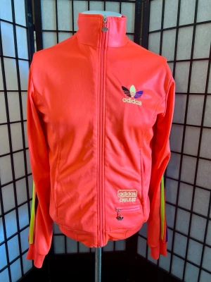 🔥 Rare Adidas Chile 62 Track Jacket 🌺 Coral 💎 Y2K - 🌺 Ovanlig Adidas Originals Chile 62 i den eftertraktade Coral-färgen. 🔥 Stor broderad Trefoil på ryggen, Chile 62-patch och klassiska 3-Stripes. Perfekt för Y2K, blokecore, terrace & streetwear. 💯 Mycket fint skick, endast några små fläckar (se bilder). 📏 P2P 48 cm | Axlar 44–45 cm | Längd 58 cm. Färgen är Coral och kan se rödare ut på vissa bilder.