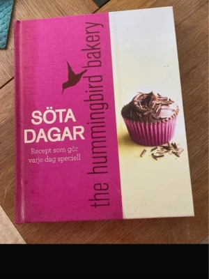 Söta dagar - The Hummingbird Bakery - En färgglad och inspirerande bakbok med hårda pärmar. Omslaget är rosa och vitt med en bild på en chokladcupcake. Innehåller massor av recept på bakverk och sötsaker, perfekt för dig som älskar att baka och vill testa nya godsaker.