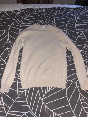 Beige cashmere - Klassisk beige cashmere tröja från John Henric. Rundad hals och ribbade muddar vid ärmslut och nederkant. Tröjan har en enkel och stilren design som passar till det mesta. Litet slitage som man inte tänker på(sista bilden)