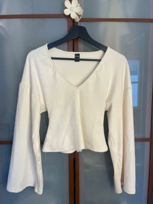 Vit v-ringad topp från SHEIN - Säljer en enkel och stilren vit topp från SHEIN i storlek XS. Toppen har v-ringning, långa ärmar och en lätt croppad passform. Perfekt att matcha med jeans eller kjol för en clean look.