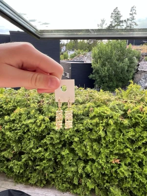 Guldiga örhängen med texten DREAM - Säljer ett par trendiga örhängen i guldton med hängande rektangulära berlocker där det står DREAM i glittriga stenar. Örhängena har små hoops och gnistrar snyggt i ljuset. Perfekta för dig som vill ha ett statement-smycke med cool vibe.  Nypris är 599kr, säljer för 199