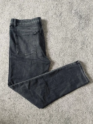 Tvättsvarta Tapered Jeans – Exklusiv - Säljer ett par stilrena tvättsvarta jeans i nyskick, endast använda ett fåtal gånger. Kraftig denim med minimal stretch ger en stabil passform och en kvalitativ känsla. Mid rise och slim/tapered fit som sitter riktigt snyggt och passar till både vardag och mer uppklädda outfits. Den tvättsvarta färgen gör dem enkla att matcha och den tidlösa designen gör dem till ett par man gärna använder om och om igen. Inga hål, fläckar eller slitage. Unikt par som är väldigt niche och går inte att hitta.