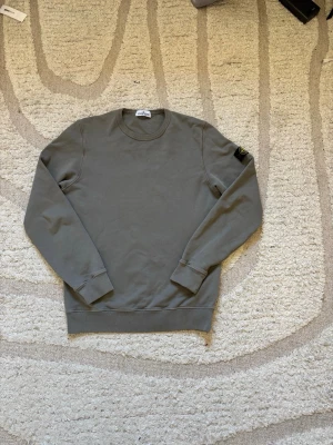 Stone Island Crewneck - Säljer en riktigt clean Stone Island crewneck i en stilren grå/beige nyans. Tröjan är i helt nytt skick utan några defekter, med den ikoniska Stone Island-kompassen på ärmen som ger den exklusiva och tidlösa looken som gjort märket så eftertraktat världen över.  📏 Storlek: 170 Junior ✅ Passar som S/M i vuxenstorlek beroende på önskad passform. ✔ Helt nytt skick ✔ Avtagbar badge på ärmen ✔ Stilren och lättmatchad färg ✔ 100% autentisk