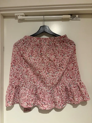 Blommig rosa volangkjol med knyt - Söt kortkjol med blommigt mönster i rosa och vitt. Kjolen har volangkant nertill och ett knytband i midjan som ger en omlott-look. Perfekt för vår och sommar.