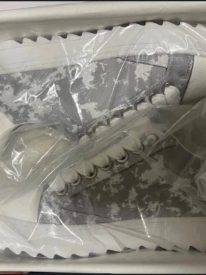 Vita och grå camo-sneakers från Numeris - Sneakers i vitt och grått med camo-mönster från Numeris. Skorna har vita snören, vit sula med taggig kant och ovandel i textil och syntet. Snygg och modern design som sticker ut med sitt unika mönster och detaljer.