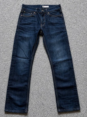 Mörkblå raka jeans med kontrastsömmar - Snygga mörkblå jeans med raka ben och klassiska kontrastsömmar. Femficksmodell med knappgylf och detaljerade bakfickor. Jeansen är tillverkade i slitstarkt denim och har en tidlös look som passar till det mesta.