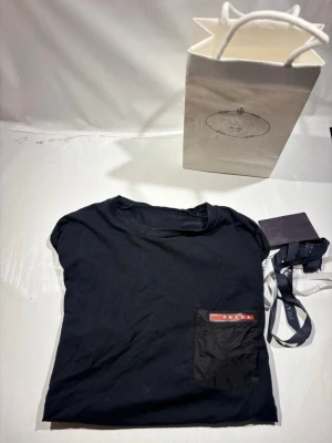 Prada T-shirt  - Hej! Säljer nu min T-shirt från märket Prada, storlek S bra skick, allt på bilden ingår. Tveka inte på att höra av dig om du har frågor eller funderingar kring tishan! 