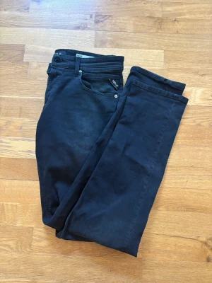 Svarta Replay Jeans - Säljer ett par svarta jeans med klassisk femficksmodell och knappgylf. Jeansen har en stilren look och är tillverkade i ett mjukt denimtyg med lite stretch för extra komfort. Perfekta till en avslappnad eller trendig outfit.