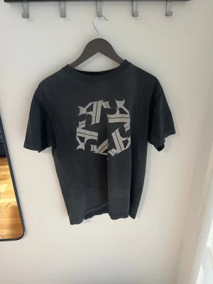 Svart Tribal USA t-shirt med tryck - Säljer en svart t-shirt från Tribal USA med ett stort grafiskt tryck i vitt på bröstet. T-shirten har rund hals och korta ärmar. Perfekt för dig som gillar streetwear och vill ha en unik look.
