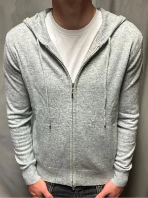 Ljusgår kashmir zip hoodie  - Lite liten på mig ja är 177En stilren ljusgrå hoodie med dragkedja framtill och huva med dragsko. Tillverkad i mjukt material och har ribbade muddar vid ärmslut och nederkant. Perfekt för en avslappnad look och enkel att matcha med jeans eller joggers.