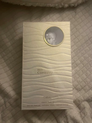 Her Confession parfym 100ml - Helt ny, oanvänd! Her Confession från Lattafa är en Eau de Parfum på 100 ml. Detta är en av de mest hållbara parfymens jag stött på under hela min livstid. Förpackningen är elegant och vit med vågigt mönster och ett runt fönster med en klassisk profilbild. Lyxig design som känns modern och stilren. 