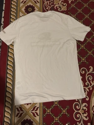 Vit Burberry t-shirt med tryck - Säljer en vit kortärmad t-shirt från Burberry med klassiskt tryck framtill i beige och brunt samt Burberry-logga. T-shirten har rund hals och normal passform. Materialet känns som mjuk bomull och är perfekt för en clean och stilren look.