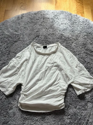 Vit kortärmad t-shirt med snörning - Säljer en vit t-shirt med korta ärmar och snörning i sidan. T-shirten har en avslappnad passform och är gjord i mjuk bomull. Perfekt till jeans eller kjol för en enkel och clean look.