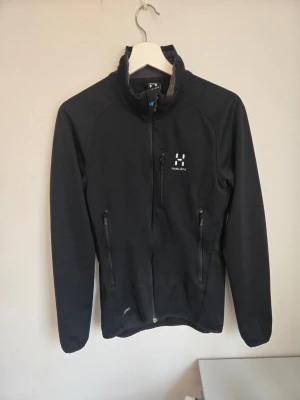 Svart softshell från Haglöfs - Svart från Haglöfs med hög krage och dragkedja framtill. Jackan har två fickor med dragkedja och diskret logga på bröstet. Perfekt för utomhusaktiviteter och har en sportig, stilren look.