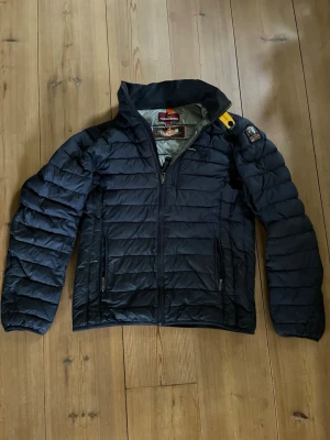 Marinblå dunjacka från Parajumpers - Snygg marinblå dunjacka från Parajumpers med gul detalj vid kragen och patch på ärmen. Jackan har quiltad design, dragkedja framtill och två sidofickor med dragkedja. Perfekt för kalla vinter/höstdagar och riktigt stilren. Använd ett fåtal gånger och har en mindre lagning vid vänster bröst (se bild 6) men syns knappt då den är lagad i samma färg!     Nypris:5399kr.   Mitt pris:2399kr