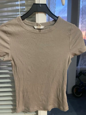 Beige ribbad kortärmad t-shirt - Säljer en enkel och stilren beige t-shirt med ribbad struktur. T-shirten har korta ärmar och rund halsringning.