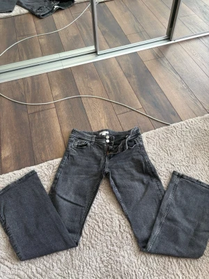 Grå svarta botcout jeans från Gina Tricot - Säljer ett par grå svarta jeans från Gina Tricot i storlek 158. Jeansen är utsvängda nertill, låg midja och två knappar i linningen. Klassiska jeans med dragkedja och snygg tvättad look. Perfekta till en avslappnad stil.