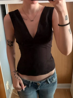 Svart v-ringad ärmlös topp - Säljer en svart, ärmlös topp med djup v-ringning och figurnära passform. Toppen är enkel och stilren, perfekt att matcha med jeans eller kjol. Materialet känns lätt och bekvämt mot huden.