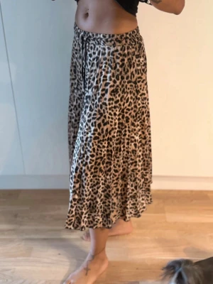 Leopardmönstrad kjol - Säljer en flowy långkjol med leopardmönster och snörning i midjan. Kjolen har beige och svarta toner och är tillverkad i ett lätt material som ger ett snyggt fall. 