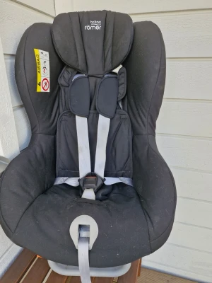Britax Römer bilbarnstol svart - Säljer en svart bilbarnstol från Britax Römer med vadderade sidor och justerbar sele. Stolen har tydliga säkerhetsmarkeringar och är designad för att ge bra stöd och komfort till barnet under bilresan. Passar i de flesta bilar och är enkel att montera.