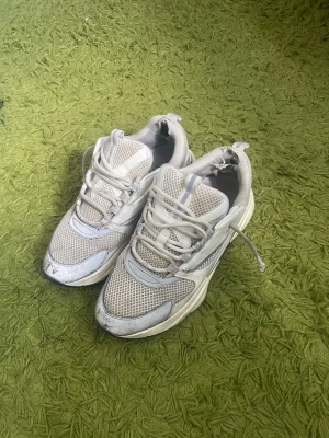 B22 vit/grå - Säljer ett par vita sneakers med mesh- och syntetdetaljer samt chunky sula. Skorna har låga skaft och klassisk snörning. Perfekta för dig som gillar en sportig och trendig look.