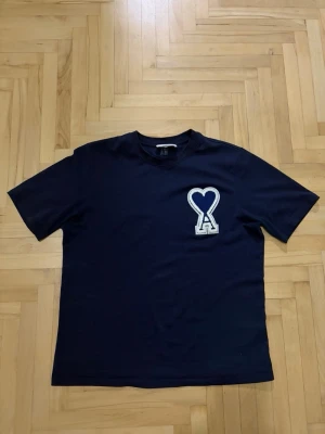 Mörkblå t-shirt från Ami Paris - Snygg mörkblå t-shirt med korta ärmar och en stor applikation på bröstet i form av ett hjärta och bokstaven A. T-shirten har en rak passform och är tillverkad i mjukt bomullstyg. Perfekt för dig som gillar stilrena plagg med en twist. 