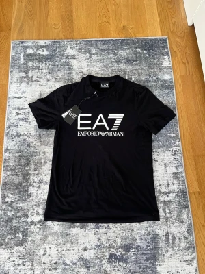 EA7 - Säljer denna EA7 t shirten eftersom den inte var min storlek och har suttit i garderoben ett tag utan använding, mycket fin , nytt skivk och perfekt till sommaren. Ettiket ingår och är köpt från Boozt för 799kr. Priset kan diskuteras!