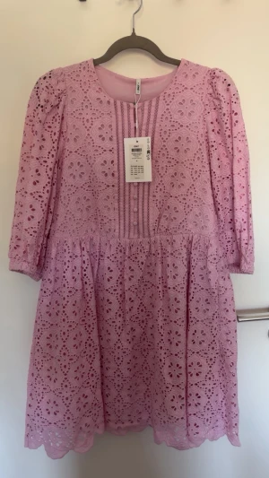 Ljusrosa spetsklänning från ONLY - Söt ljusrosa kortklänning från ONLY med broderad spets, trekvartsärm och dekorativa knappar framtill. Klänningen har rund halsringning och volangkant nedtill. Perfekt för sommarens alla tillfällen.