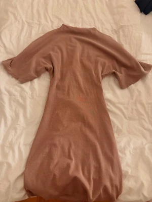 Beige kortklänning från Gina Tricot - Ljuset gör klänningen mörkare. Kortklänning i mjukt beige tyg från Gina Tricot. Klänningen har korta ärmar och en enkel, rak passform med rund hals. Perfekt för en avslappnad och stilren look.