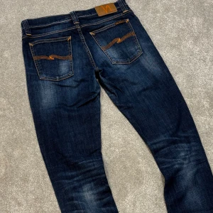 Nudie Jeans - Tja! Säljer dessa riktigt feta mörblå/blå Nudie jeans med schysst tvätt! Slimfit passform. Jeansen är i bra skick utöver ett litet hål i höger ficka, enkel fix dock. Size 28/32 men lite stretch så kan passa upp till 30 i i midja lätt. Skriv vid fler frågor!
