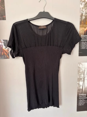 Svart ribbad mesh-topp - Säljer en svart topp med ribbad nederdel och mesh-tyg upptill samt på ärmarna. Toppen har rund halsringning och korta ärmar. Perfekt för dig som gillar en stilren men edgy look.