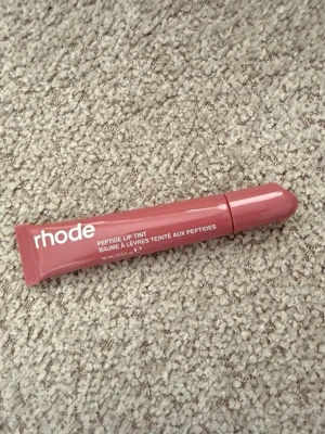 rhode Peptide Lip Tint Salty Tan - Säljer ett rhode Peptide Lip Tint i färgen Salty Tan. Läppbalsamet kommer i en smidig tub med skruvlock och har en mjuk, brunrosa ton. Perfekt för dig som vill ha återfuktade läppar med en hint av färg. Innehåller peptider för extra vård. Endast testad på handen
