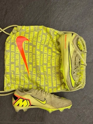 Gula  Nike Mercurial fotbollsskor elit  - Säljer ett par gula Nike Mercurial fotbollsskor elit med svarta och neonröda detaljer. Skorna har snörning, låg profil och dobbar för spel på gräs. Tillverkade i syntetmaterial för bra grepp och lätt känsla. Medföljer matchande Nike-påse.