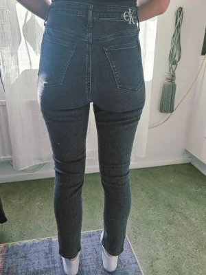 Mörkgrå high waist jeans Calvin Klein - Säljer ett par svarta high waist jeans från Calvin Klein. Jeansen har smal passform, klassiska fem fickor och Calvin Klein-logga på bakfickan. Materialet är stretchigt denim som sitter snyggt och bekvämt. Perfekta till en avslappnad men ändå stilren look.Ej retur. 